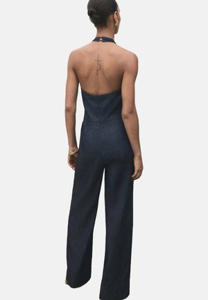 Denim jumpsuit with a fitted bodice and wide-leg trousers, featuring a halter neck and backless design. Dark wash and smooth texture.