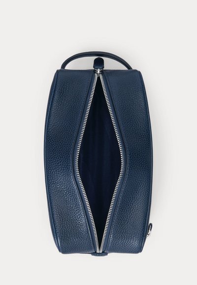 Ορθογώνια τσάντα από δέρμα σε ναυτικό μπλε χρώμα με υφή κόκκων, μερικώς ανοιχτό ασημένιο φερμουάρ και λαβή μεταφοράς στο πάνω μέρος σε λευκό φόντο.