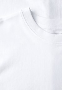 Bílé bavlněné tričko s kulatým výstřihem, s hladkou texturou a krátkými rukávy. Jemné švy podél límce a těla.