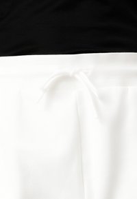 White pants with a textured fabric, featuring a drawstring waist and pleated details, paired with a black top cut off at the waist.