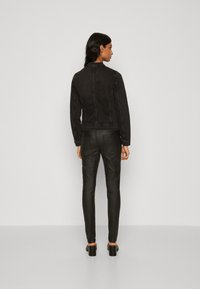 Svart denimjakke med lange ermer, en tettsittende design og synlig søm. Kombinert med svarte slim-fit bukser og sko med blokkhel.