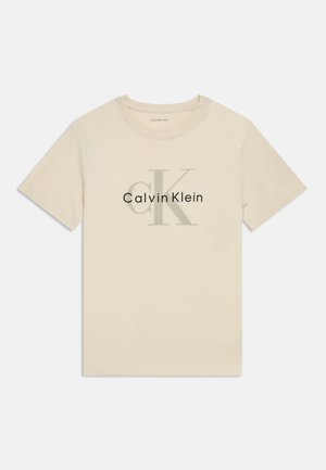Bež kratka majica s okruglim izrezom i kratkim rukavima, s velikim svijetlosivim natpisom "cK" i logotipom "Calvin Klein" smještenim u sredini sprijeda.