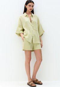 Lichtgroen textuurshirt met een kraag en knopen, gecombineerd met bijpassende shorts. Gebroken bruine sandalen met metalen accenten.