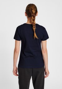 Marineblå bomulls t-shirt med kort ärm, rund halsringning och en slät yta, sedd bakifrån, tillsammans med mörka byxor.