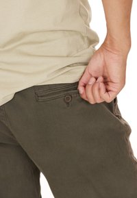 Olivgröna byxor med en texturerad yta, med en sidoficka som har en brun knapp. En beige skjorta syns delvis ovanför.