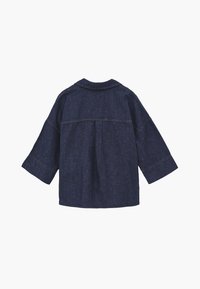 Mørkeblå denimjakke med brede ærmer og et skuldersøm på tværs af den øverste ryg, set bagfra.