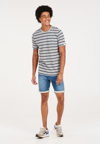 Camiseta de rayas de manga corta gris con líneas azul marino, combinada con pantalones cortos de mezclilla con dobladillos enrollados y acentos de color claro.