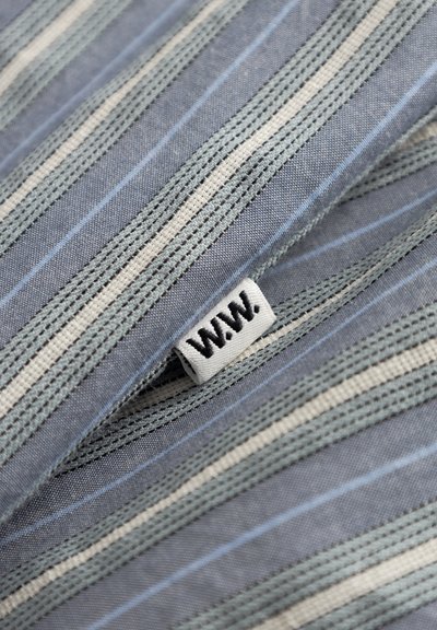 Tkanina s črtami v modri, sivi in krem barvi. Viden je tkan etiketa z napisom "W.W." v črni barvi. Mehka tekstura in lahka zasnova.