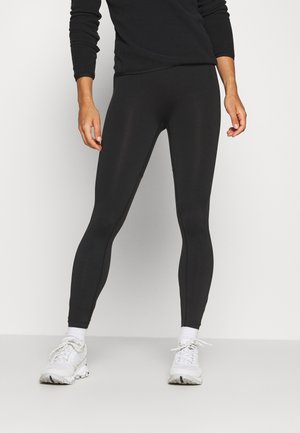 Leggings noirs extensibles avec une texture lisse, un design ajusté et une taille haute. Associés à des chaussures de sport blanches et des chaussettes.