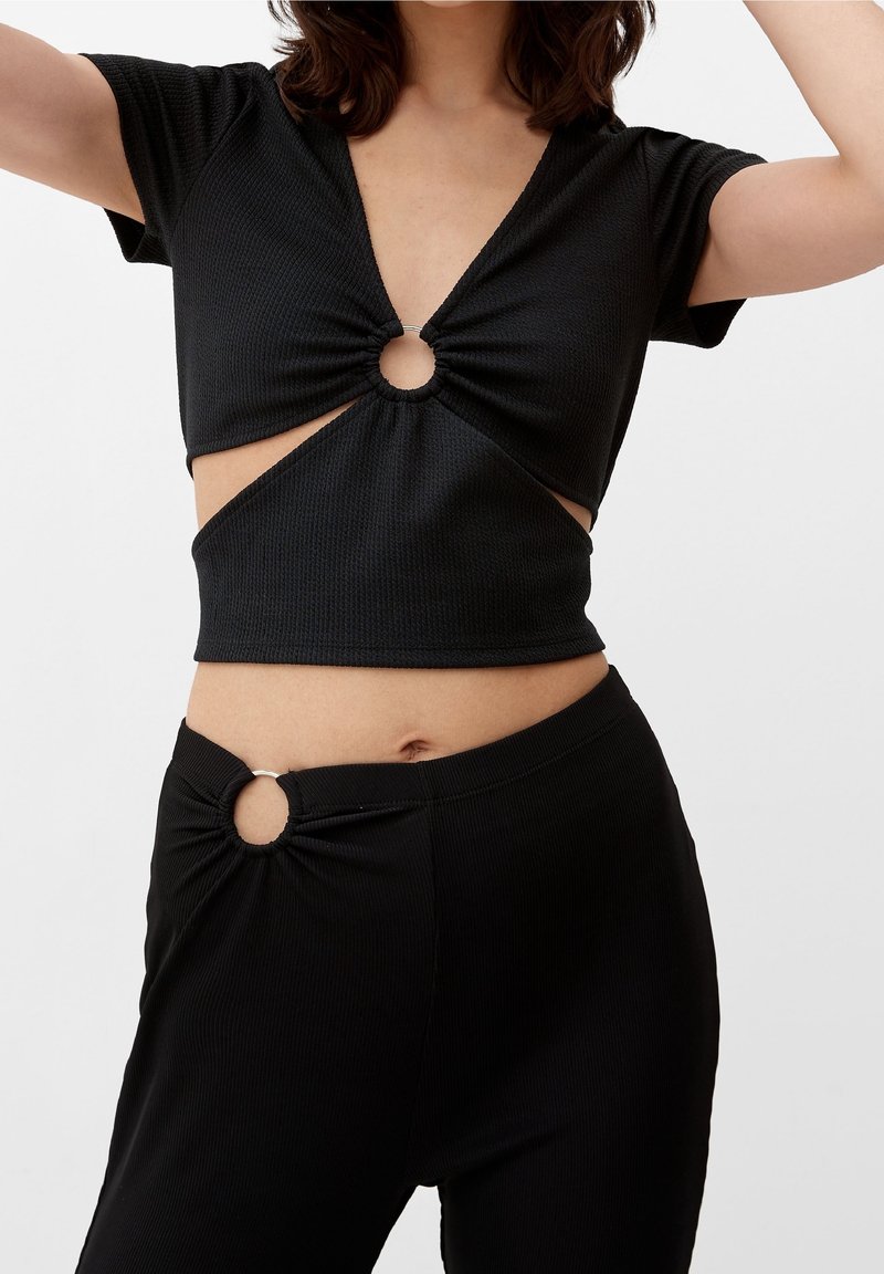 Černý žebrovaný pletený crop top s krátkými rukávy a hlubokým výstřihem ve tvaru V, s kulatým výřezem ve středu, doplněný kalhotami s vysokým pasem.
