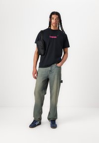 Black t-shirt with pink "FORMER" logo, loose blue denim jeans, and blue sneakers with three white stripes; small black crossbody bag.