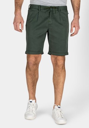 Groene katoenen shorts met een aansluitend ontwerp, opgerolde zomen en een ritssluiting aan de voorkant. Draagt met witte sneakers.