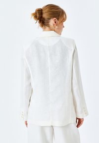 Witte linnen blazer met een gestructureerd ontwerp, voorzien van een enkele split, lange mouwen en crèmekleurige knopen op de manchetten. Glad, textuurstof.