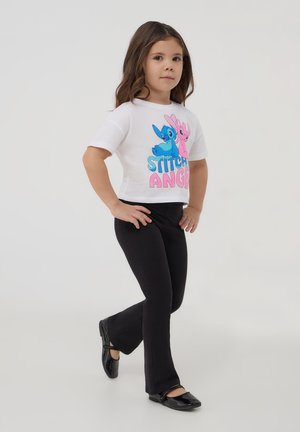 T-shirt bianco a maniche corte con personaggi dei cartoni animati in blu e rosa, abbinato a leggings neri svasati e ballerine nere.