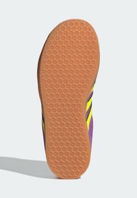 Kolorowa podeszwa sportowego buta z teksturowaną pomarańczową gumową powierzchnią o geometrycznym wzorze, otoczona fioletowo-żółtą cholewką.