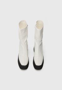 Botine albe până la gleznă, cu un design ajustat, realizate din piele netedă, având o talpă din cauciuc negru și închidere cu fermoar lateral pentru o purtare ușoară.