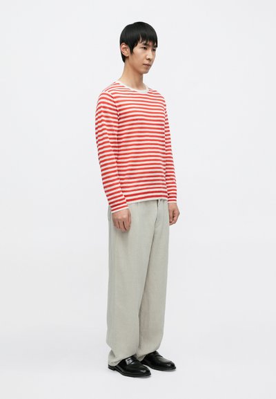 Κόκκινο και λευκό ριγέ πουκάμισο με μακριά μανίκια και στρογγυλή λαιμόκοψη, σε συνδυασμό με ανοιχτό γκρι, φαρδιά παντελόνια και μαύρα παπούτσια.