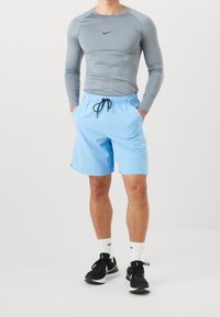 En atletisk person som bär en tät grå långärmad tröja, ljusblå shorts med dragsko, vita Nike-strumpor och svarta löparskor.