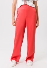 Rode satijnen broek met wijde pijpen, een gladde textuur en een elastische tailleband, gedragen met witte vetersneakers.