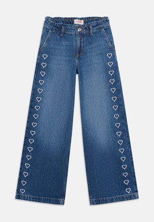 Jeans bleu à jambes larges avec des cœurs blancs brodés en vertical le long des coutures extérieures des deux jambes.