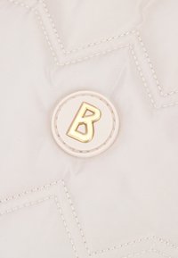 Tessuto bianco trapuntato con cuciture a zigzag e un distintivo circolare con un emblema d'oro a forma di "B". Texture liscia e leggero lucore.