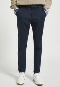 Granatowe chinosy wykonane z gładkiego materiału; dopasowany krój, z bocznymi kieszeniami i szlufkami na pasek, zestawione z białymi trampkami.