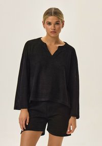 Czarna siateczkowa bluzka z dekoltem w serek i długimi rękawami, w zestawie z dopasowanymi szortami. Oba elementy mają luźny krój i teksturowany wzór.