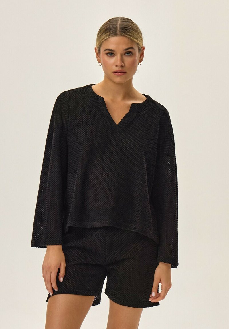 Czarna siateczkowa bluzka z dekoltem w serek i długimi rękawami, w zestawie z dopasowanymi szortami. Oba elementy mają luźny krój i teksturowany wzór.