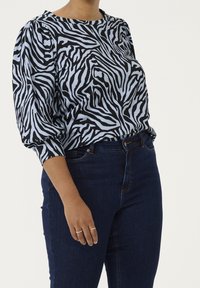 Black and light blue zebra-striped blouse with puffed sleeves; worn with dark blue jeans. The fabric has a textured appearance.