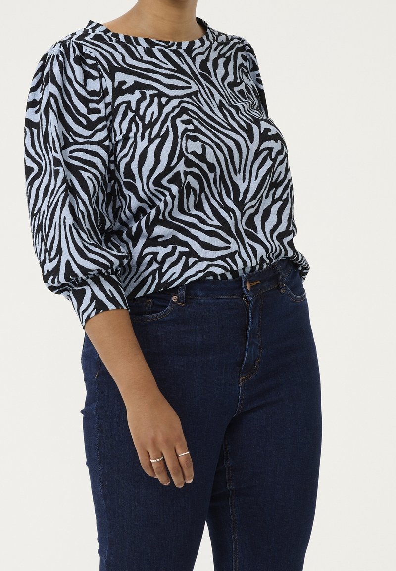 Black and light blue zebra-striped blouse with puffed sleeves; worn with dark blue jeans. The fabric has a textured appearance.