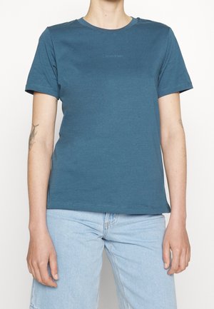 Sininen puuvillapaita lyhyillä hihoilla, pyöreällä kaula-aukolla ja hienovaraisella logo-printillä rinnan keskellä. Sujuva kangas ja normaali istuvuus.