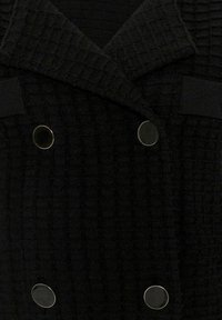 Svart stickad kappa med ett strukturerat mönster, som har en dubbelknäppt design och metallknappar. Bred krage och strukturerade axlar.