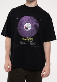 Black t-shirt featuring a large purple vinyl record graphic, with white label details and textual elements related to "Purple Rain."