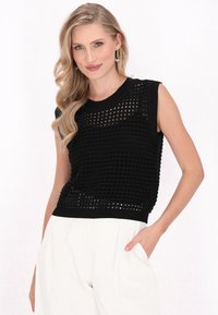 Top senza maniche lavorato a maglia nera con un design testurizzato a trama aperta. Presenta scollo rotondo e orlo a coste, abbinato a pantaloni bianchi a vita alta.