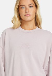 Light pink sweatshirt made from soft fabric, featuring a round neck and long sleeves. It has an embroidered "Billabong" logo on the front.