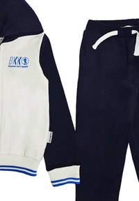 Completo sportivo a due pezzi composto da una felpa bianca e blu navy con zip e dettagli blu, e pantaloni della tuta blu navy con cordino in vita.