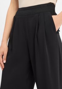 Black trousers with a wide leg, featuring a waistband with a ribbed texture, side pockets, and subtle pleats for added detail.