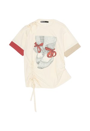 Cream-colored short-sleeve shirt with red and beige sleeve cuffs, ruched side ties, and a graphic of feet wearing ballet shoes with red ribbons.