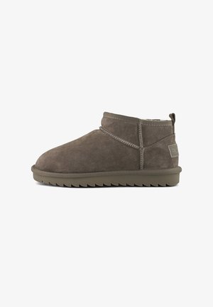 Bottine en daim marron avec semelle en caoutchouc épaisse, couture visible et tirant au niveau du talon, présentée en profil latéral sur un fond blanc.