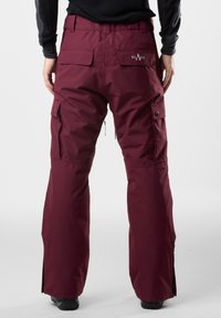 Bordowe spodnie snowboardowe o prostym kroju, z kieszeniami cargo, wentylacją na suwak oraz logo na plecach. Wykonane z materiału odpornego na wodę.