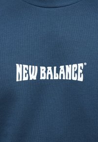 Ύφασμα σε ναυτικό μπλε με λευκό, στυλιζαρισμένο κείμενο "NEW BALANCE" τυπωμένο στο κέντρο.