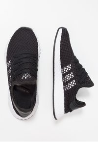 Svarta träningsskor med ovandel i mesh, med vita accenter och en texturerad sula. Snörningsdesign med rundad tå och lätt konstruktion.