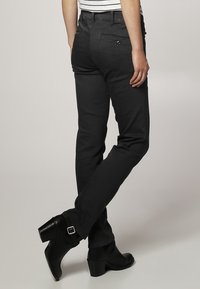 Vaqueros negros ajustados con una textura suave, con un bolsillo trasero y una cintura de altura media. Llevados con botas de tacón negras.