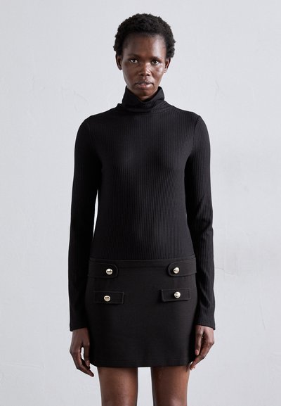 Pull en maille côtelée noir avec col roulé et manches longues ; design ajusté. Associé à une mini-jupe noire avec des détails en boutons dorés sur les poches.
