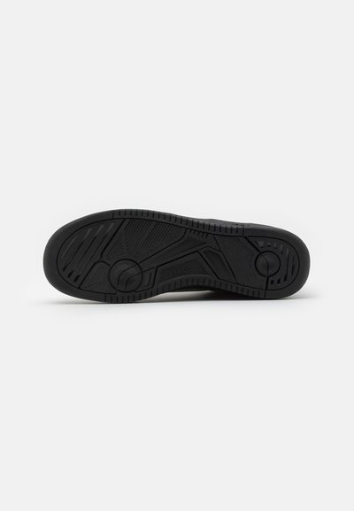 Black rubber sneaker sole with textured tread pattern, featuring circular and angular details. Smooth finish with a brand logo embossed.