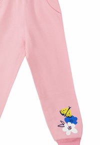 Rosa Baumwoll-Sweatpants mit Seitentaschen. Mit einem gelben Schmetterling und blauen sowie weißen Blumenmustern nahe dem Saum.