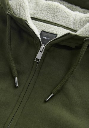 Olivgrüne Zip-Hoodie mit einer weichen Creme-Sherpa-Fütterung, Metallschneider und Zugbändern. Besitzt ein Etikett mit der Aufschrift "NEXT" im Inneren.