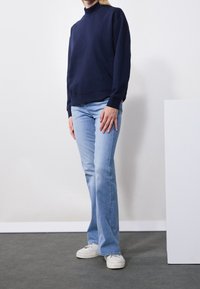 Felpa navy a collo alto con vestibilità ampia, abbinata a jeans azzurri a zampa d'elefante e sneakers bianche. Design semplice e texture del tessuto morbida.