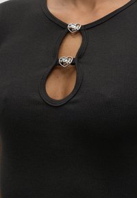 Κοντινό πλάνο μαύρου ριμπ τοπ με δύο καρδιαρά ασημένια κούμπωμα που συνδέουν το ύφασμα στο άνοιγμα στο στήθος.