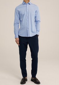 Camisa de manga larga azul con cuello abotonado, confeccionada en una tela suave, combinada con pantalones navales y mocasines negros.